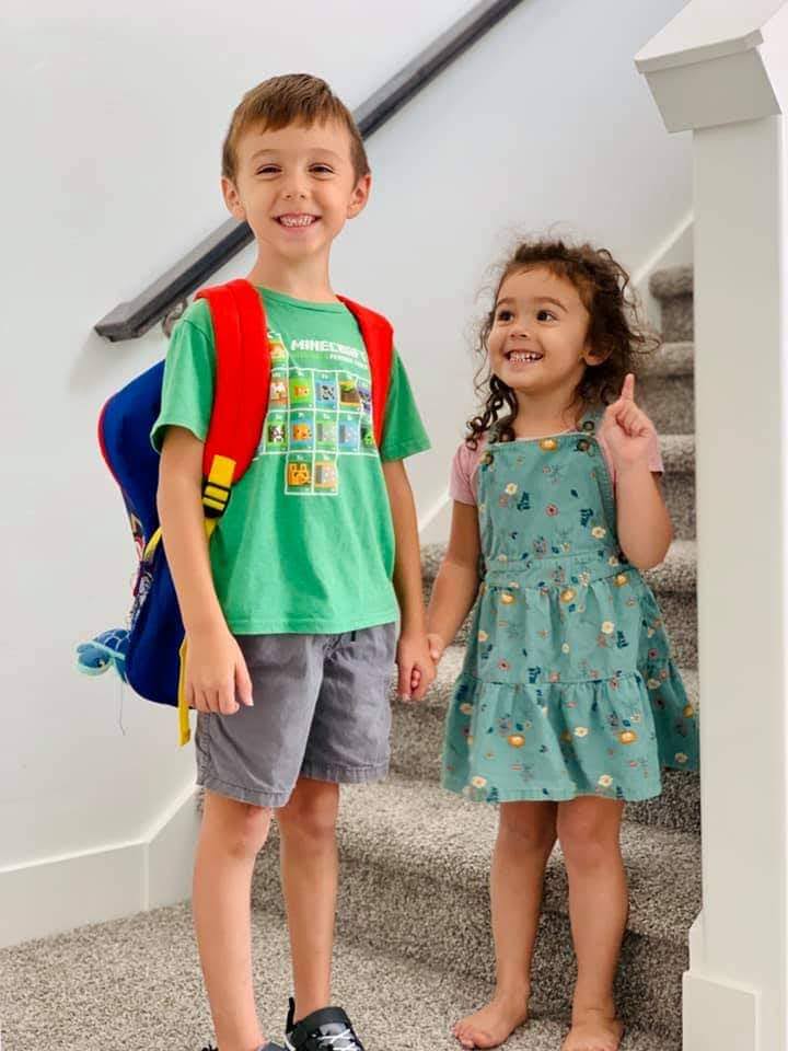 A boy on his first day of school standing for a picture with his younger sister.