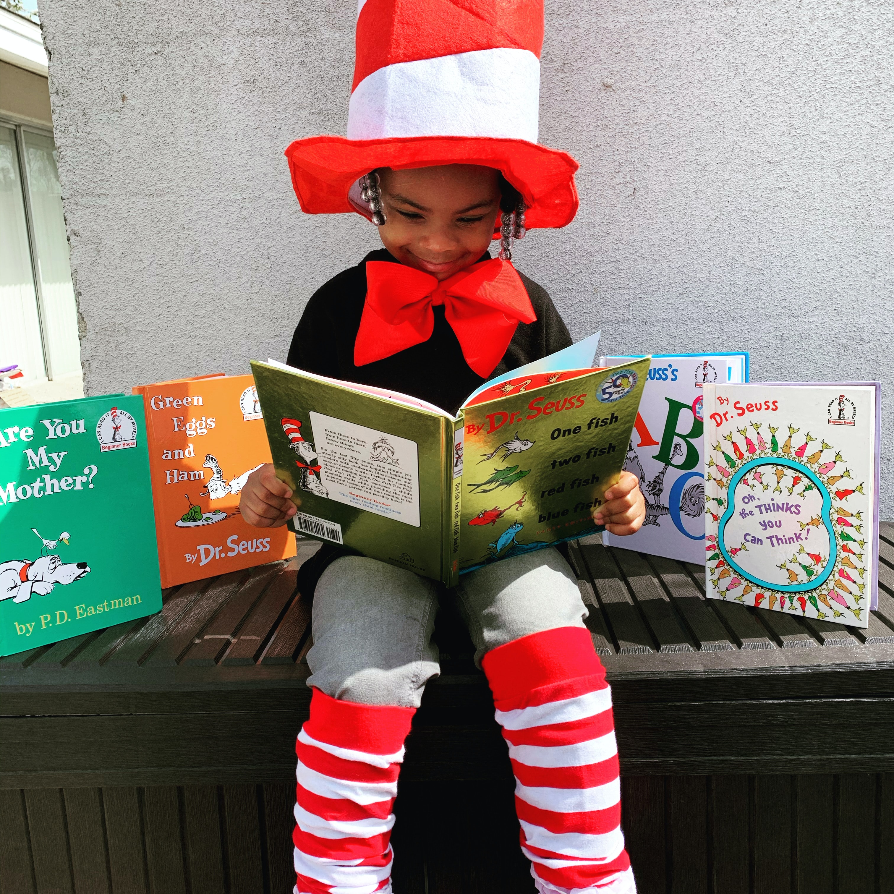 Child in Dr. Seuss Costume reading a Dr. Seuss book.  He is surrounded by other Dr. Seuss books as well.