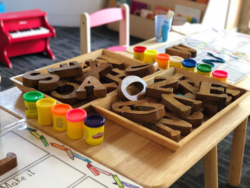 Wooden letters and playdough containers on a table.